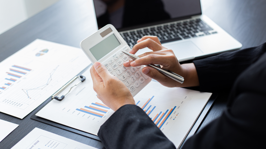 person typing on a calculator with paper work on the table and a laptop open on a table - adam tobin law